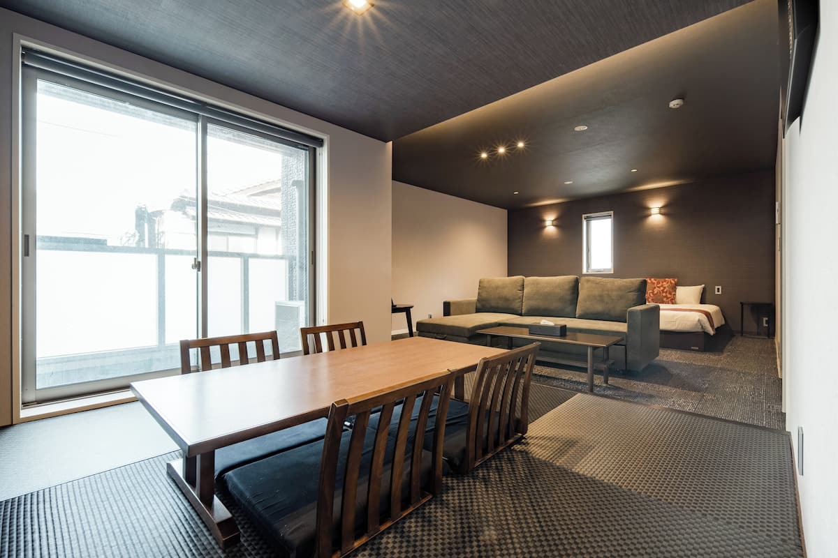A modern hotel room with a dining area, a sofa, and a large window.
