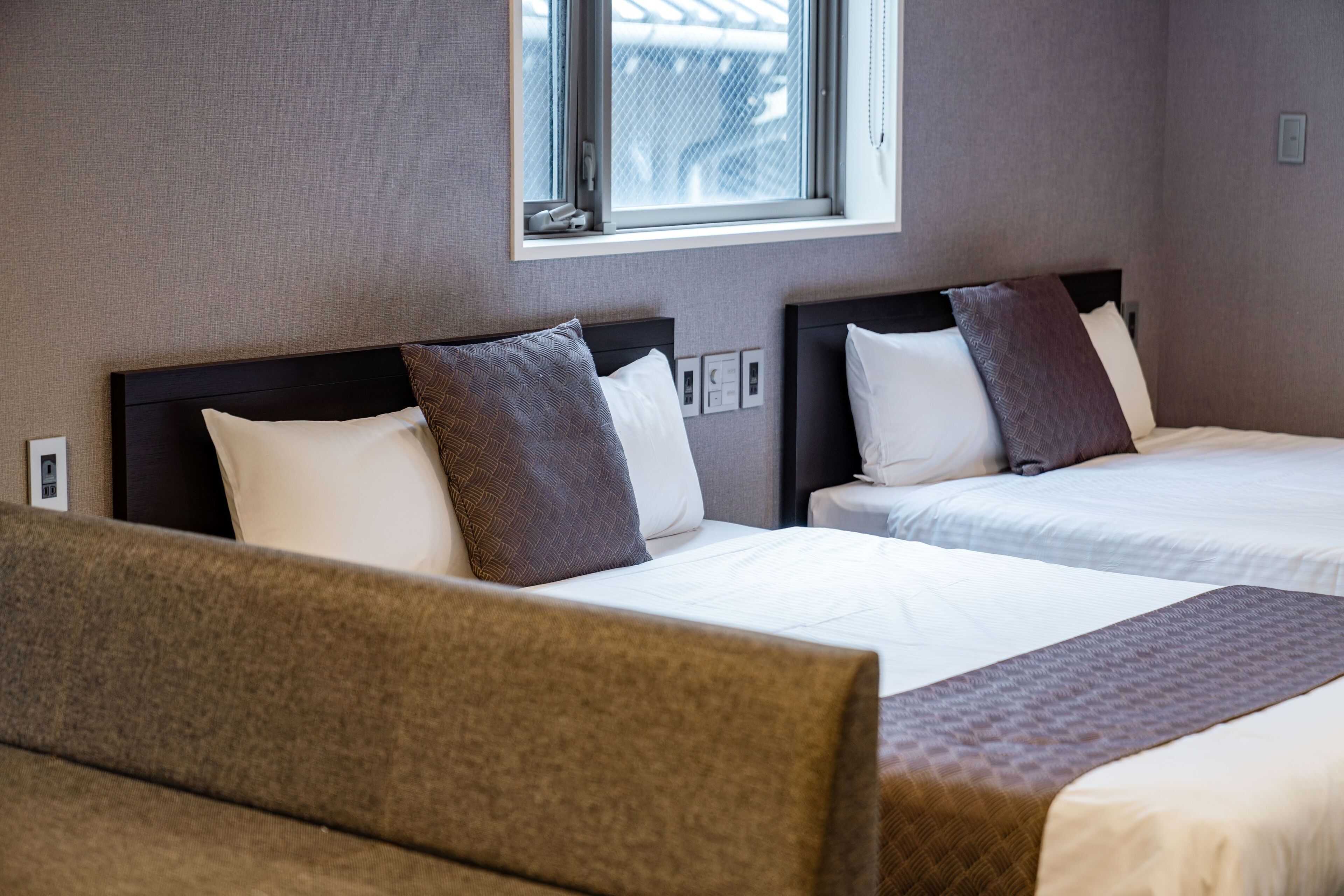 A hotel room with two beds, a window, and a view of the outside.