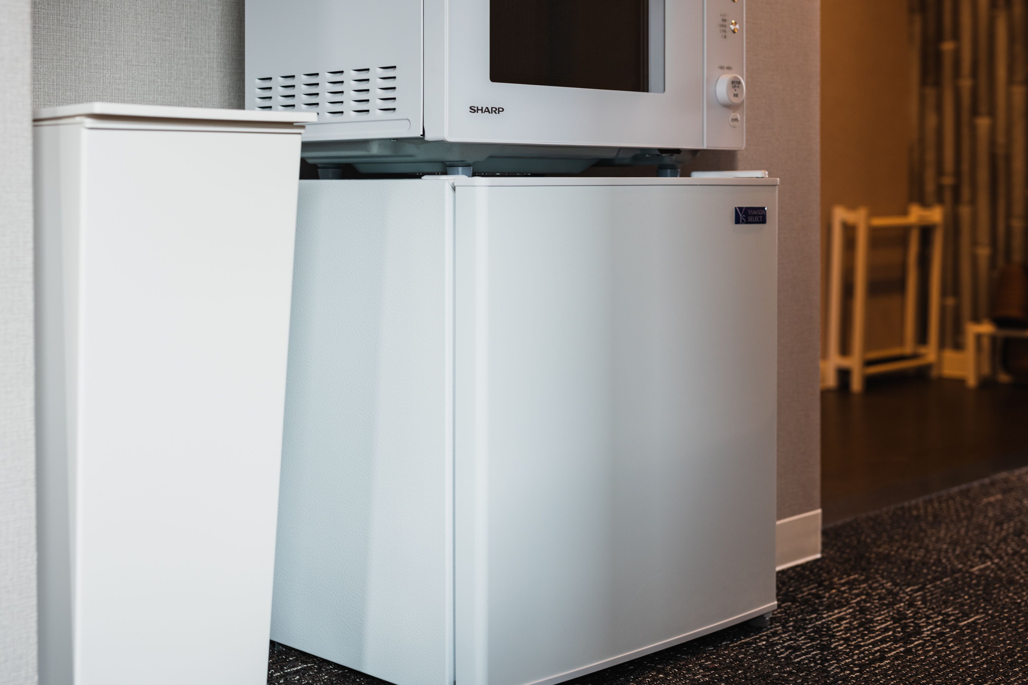 Un refrigerador compacto con un microondas incorporado encima, ubicado contra una pared en una habitación de hotel.