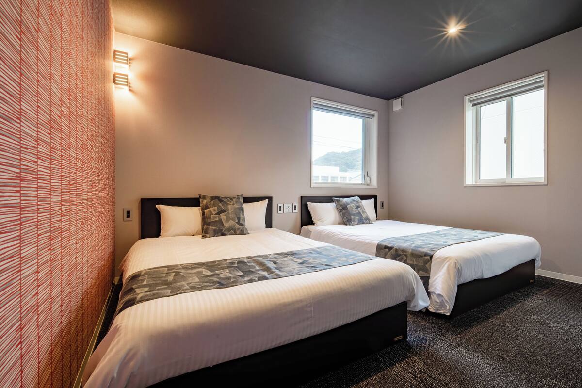 A hotel room with two beds, a patterned wall, and a window.