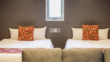Ein Hotelzimmer mit zwei Betten, jedes mit einem blumigen Kopfkissen, einem Fenster darüber und einer wandmontierten Steuerung.