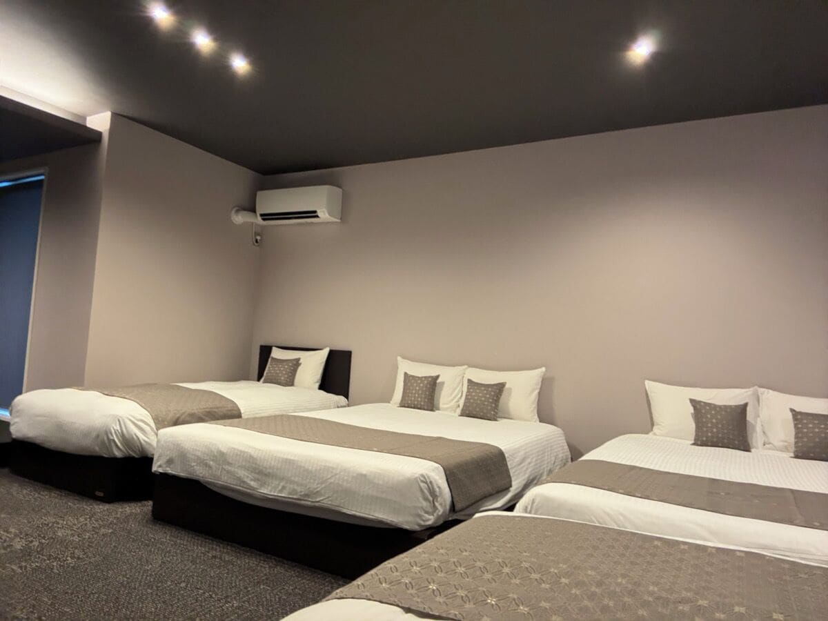 A hotel room with three beds, a ceiling air conditioner, and a carpeted floor.