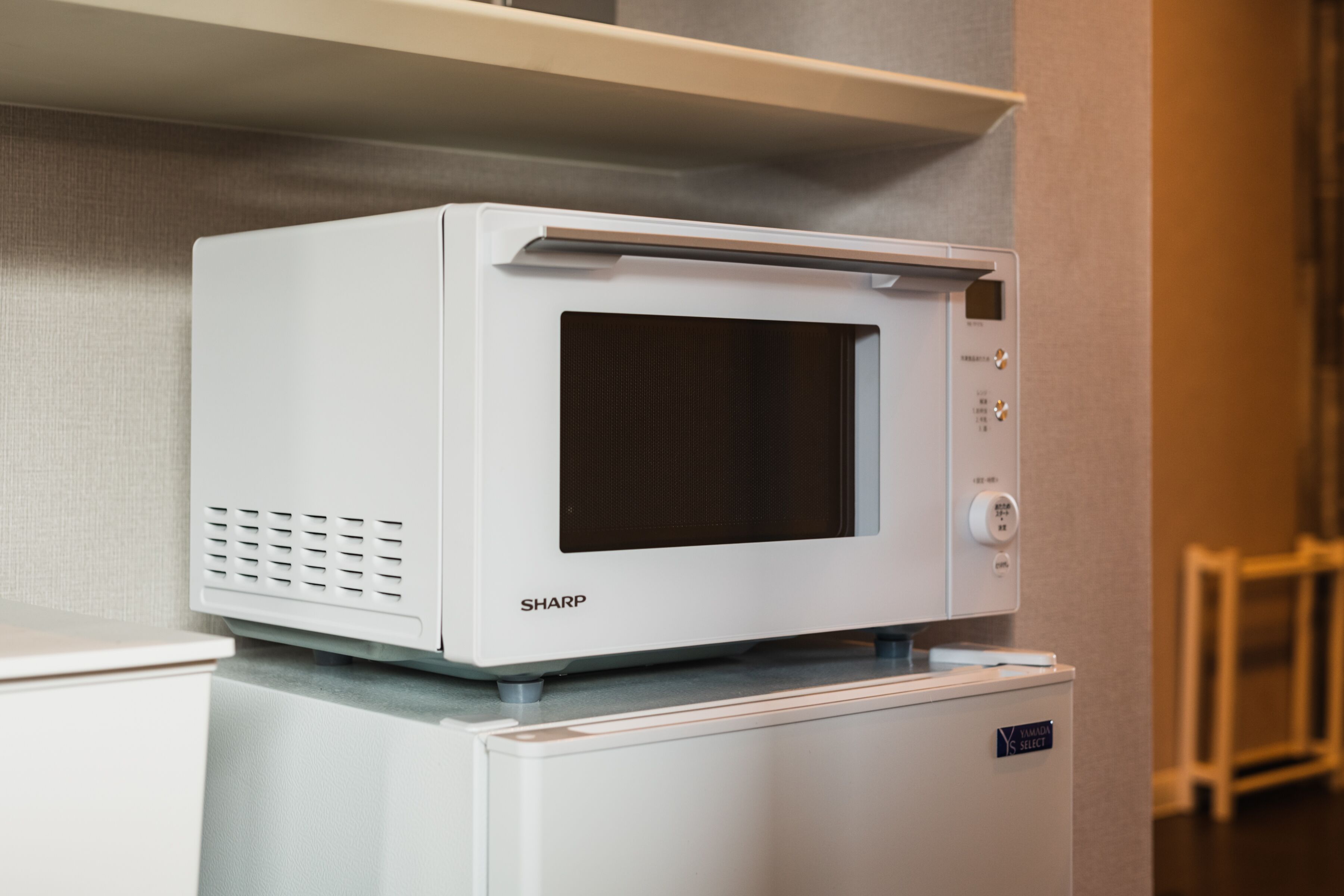 A white Sharp microwave on top of a white refrigerator in a kitchen.