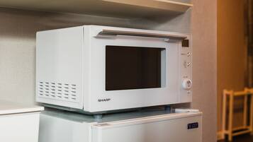 A white Sharp microwave on top of a white refrigerator in a kitchen.