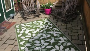 Un patio con dos sillas de mimbre, una maceta de flores rosadas y un tapete verde y blanco estampado.