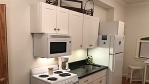 Una cocina compacta con armarios blancos, un microondas, una estufa y un refrigerador.