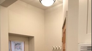 Una habitación pequeña y limpia con una puerta blanca, un perchero, un calentador y un cubo de basura.