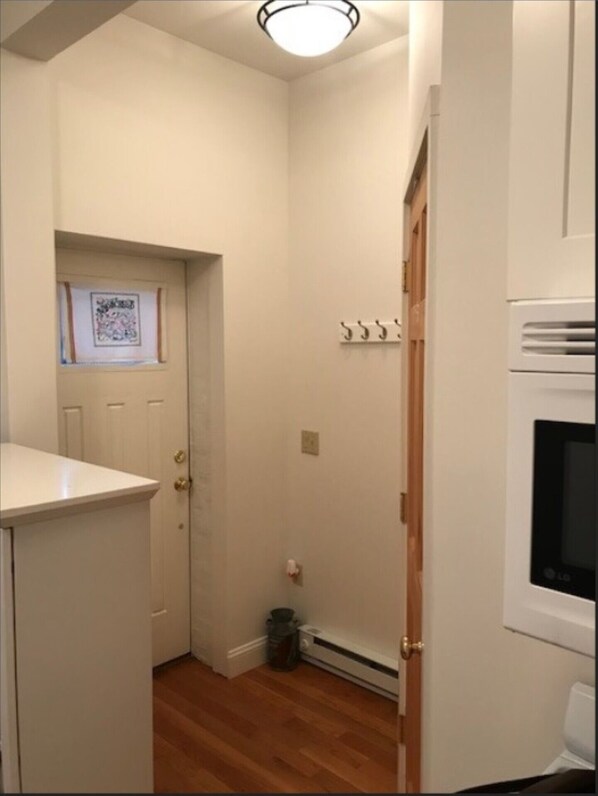 A small, clean room with a white door, a coat rack, a heater, and a trash can.