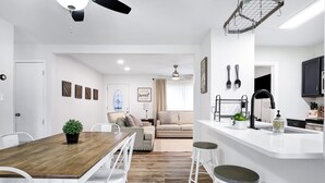 Una cocina moderna con una isla central, muebles blancos y un comedor con mesa de madera y sillas blancas.