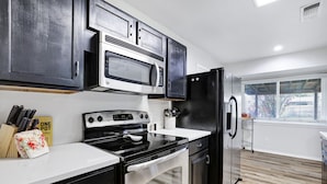 Una cocina moderna con electrodomésticos de acero inoxidable, gabinetes negros y encimera blanca.