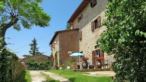 A stone building with a garden path leading to a blue umbrella. - Cosy apartment in villa for 2 people with WIFI, pool, terrace, pets allowed and panoramic view (Pulicciano)