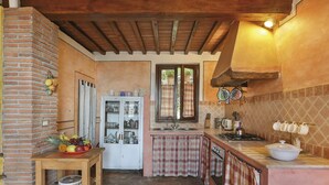 Une cuisine rustique avec des murs en briques apparentes, des poutres en bois, un mur recouvert de carreaux et une table en bois sur laquelle sont disposés des fruits.