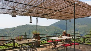 Un espace de restauration en plein air avec une table et des chaises, une lanterne suspendue et une vue sur des collines verdoyantes.