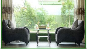 A room with two wicker chairs facing a window with a view of greenery and a building. - Hotel Bella (Mandalay)