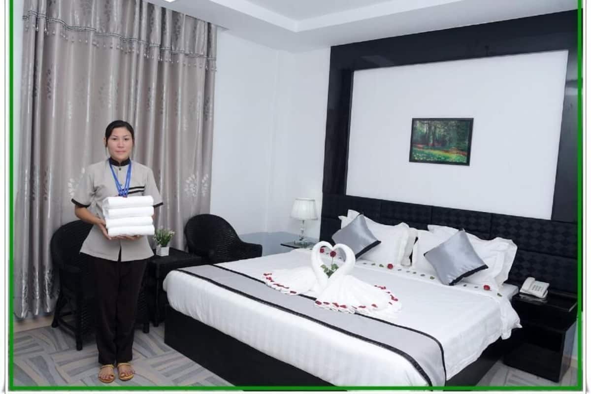 Habitación de hotel con una cama bien hecha, un cuadro en la pared y una persona sosteniendo toallas dobladas.