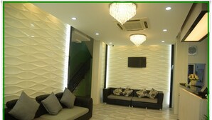 A reception area with a sofa, patterned wall, chandelier, and a reception desk. - Hotel Bella (Mandalay)