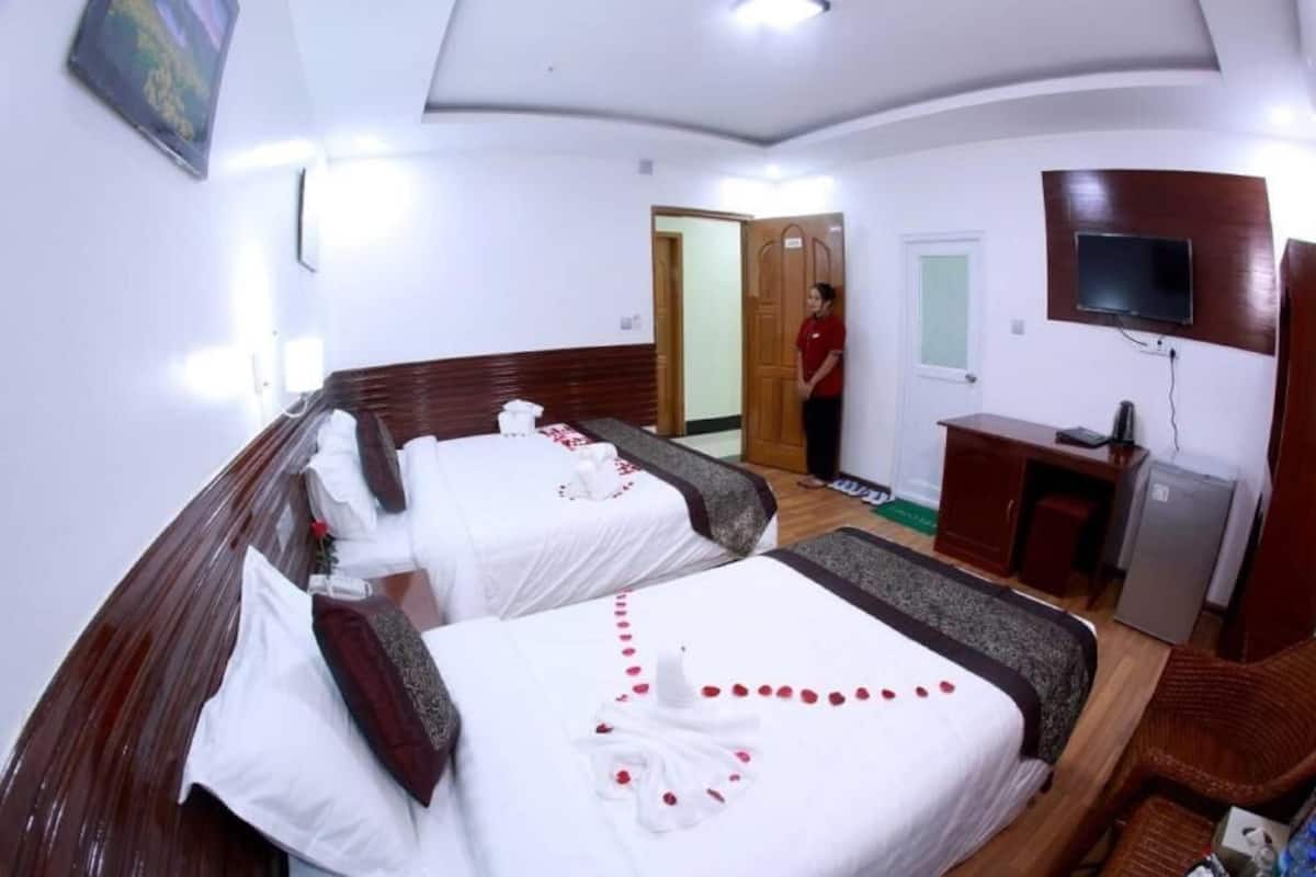Habitación de hotel con dos camas, un escritorio, un televisor y un refrigerador pequeño.
