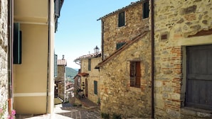 Une ruelle pavée bordée de bâtiments traditionnels, un ciel dégagé et une vue lointaine sur une colline.