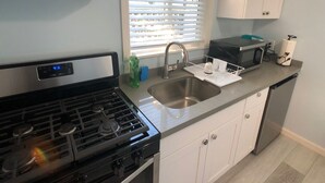 A modern kitchen with a stainless steel sink, a built-in microwave, and a dishwasher. - Charming Cozy Centralize Studio (San Mateo)