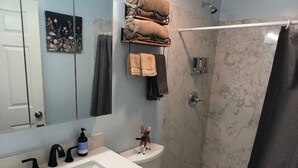 A bathroom with a white sink, dark gray cabinets, a white toilet, a shower with a glass door, and a towel rack with folded towels. - Charming Cozy Centralize Studio (San Mateo)
