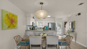 A dining area with a wooden table and four chairs, a hanging light fixture, and a large flower painting on the wall.