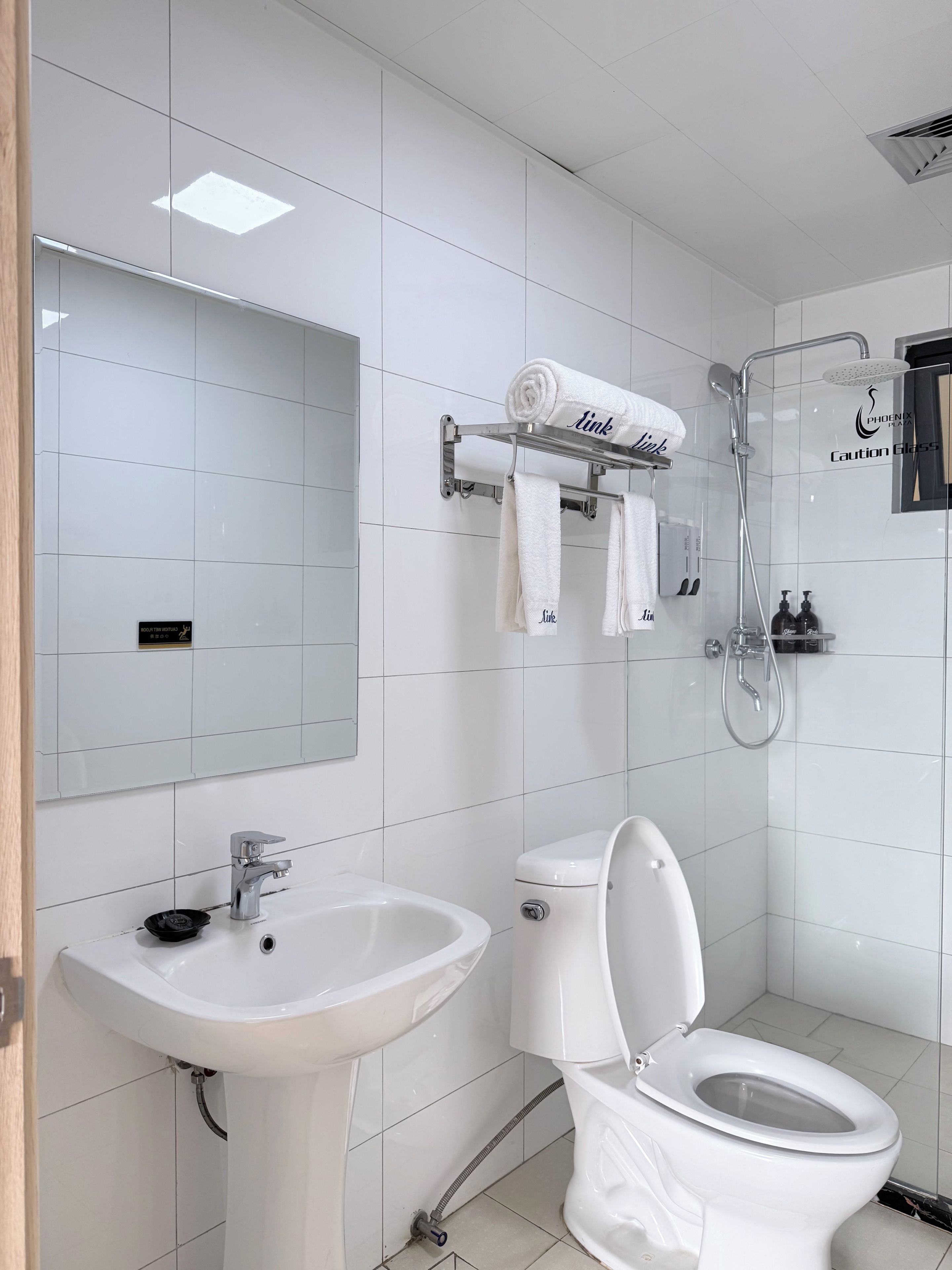A modern bathroom with a white sink, toilet, and shower. There are towels hanging on a rack and a mirror above the sink.