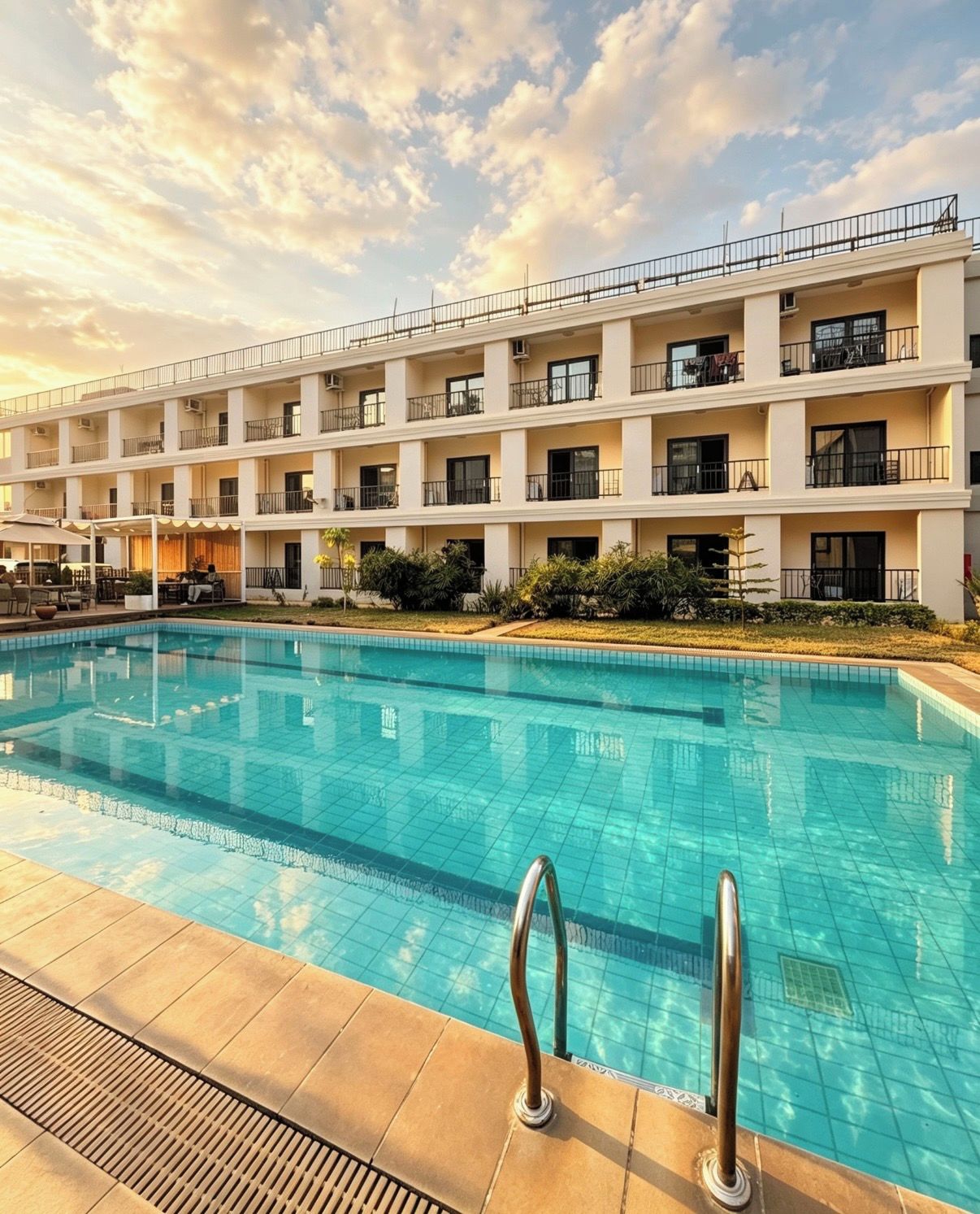 A multi-story hotel with a swimming pool, outdoor seating, and a clear sky.