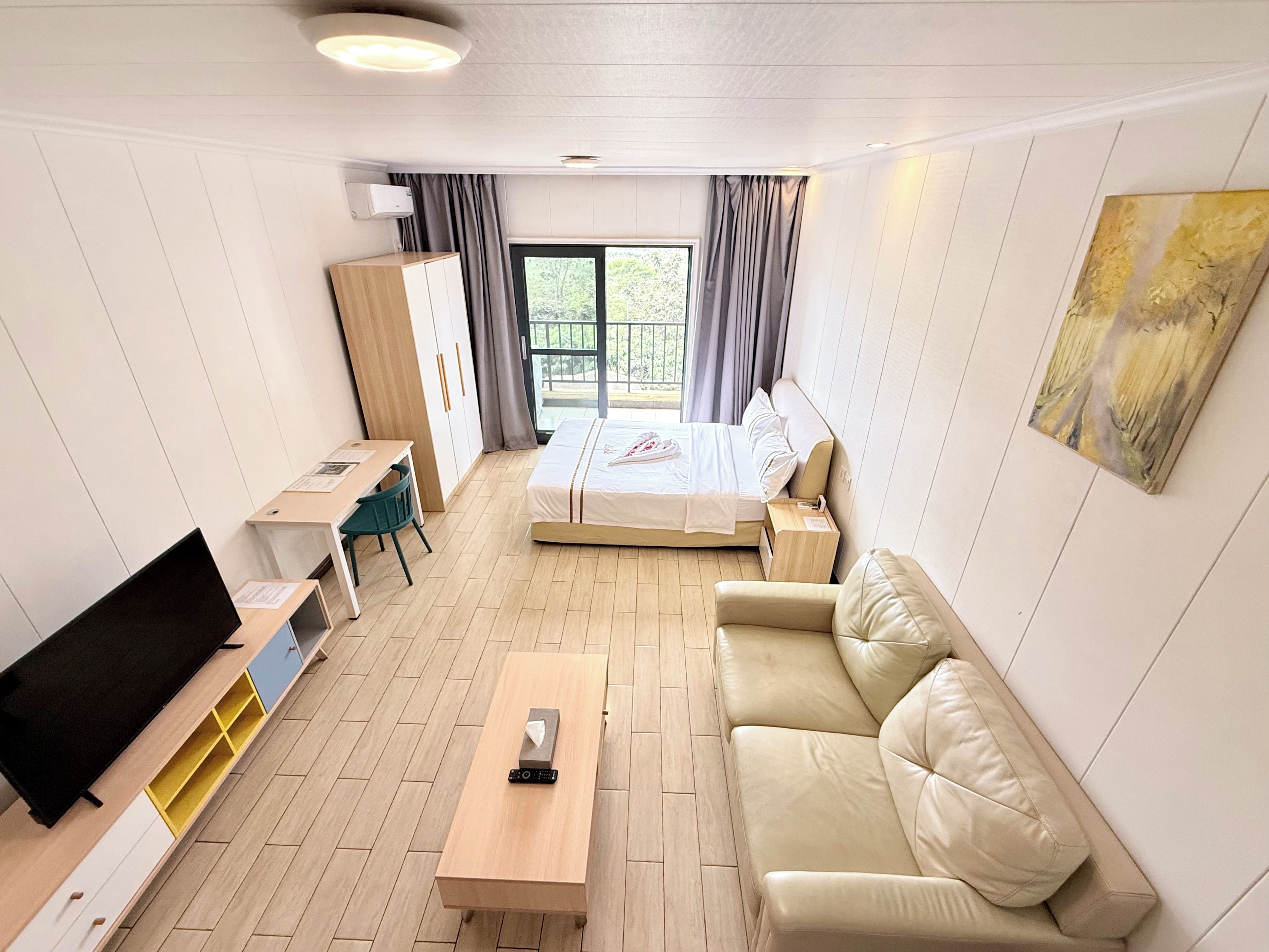 Una habitación de hotel con cama, sofá, escritorio, televisión y ventana con cortinas.