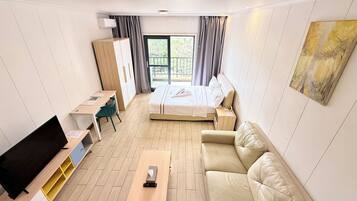 Una habitación de hotel con cama, sofá, escritorio, televisión y ventana con cortinas.