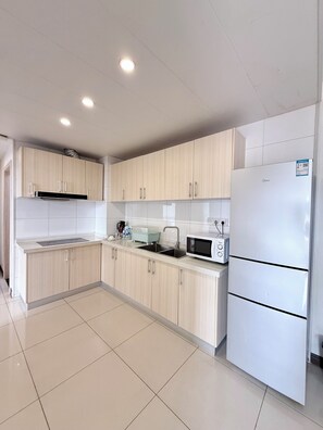 A modern kitchen with light wood cabinets, a white refrigerator, and a microwave.