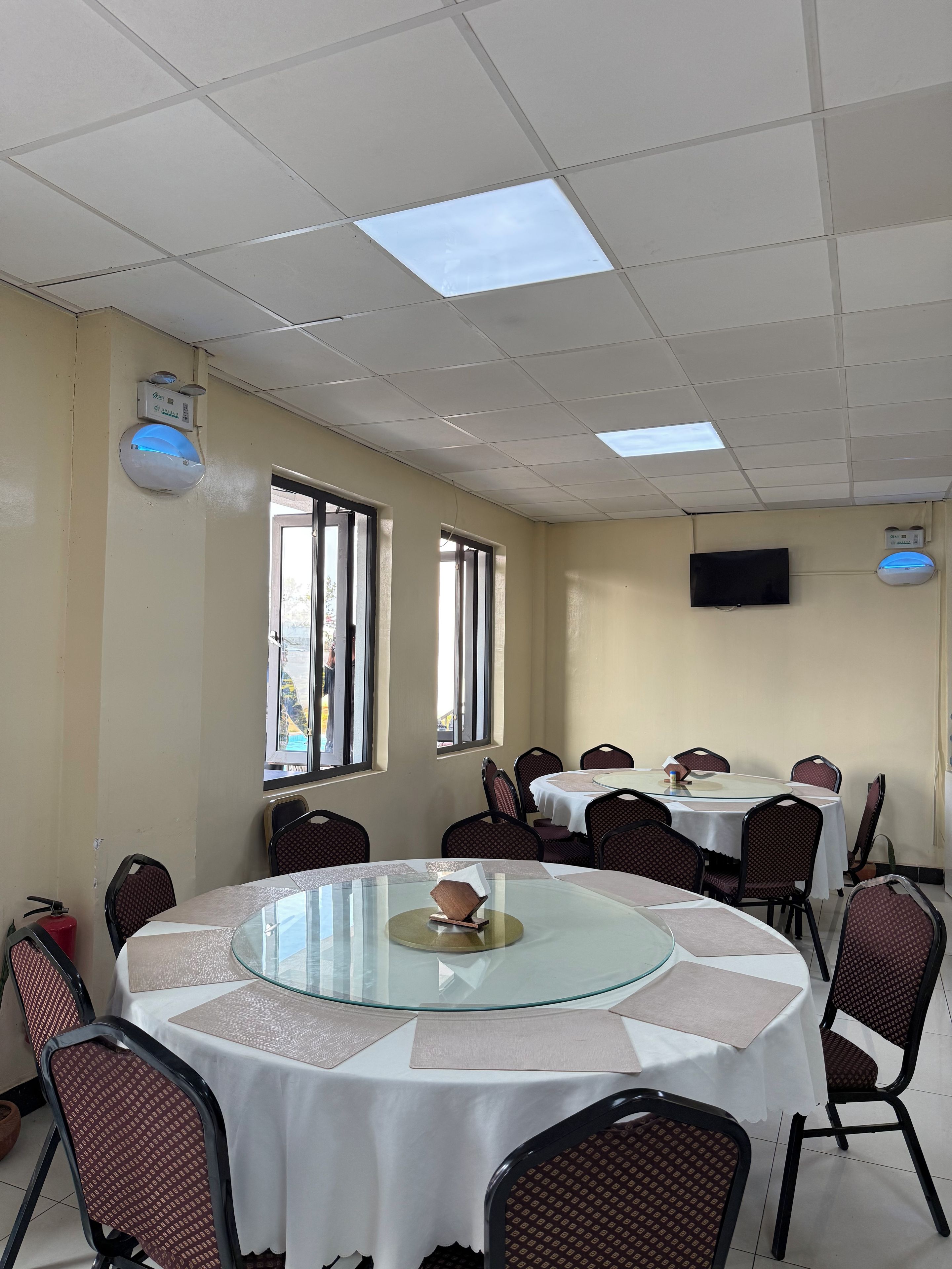 A conference room with round tables, chairs, a fire extinguisher, and a television on the wall.
