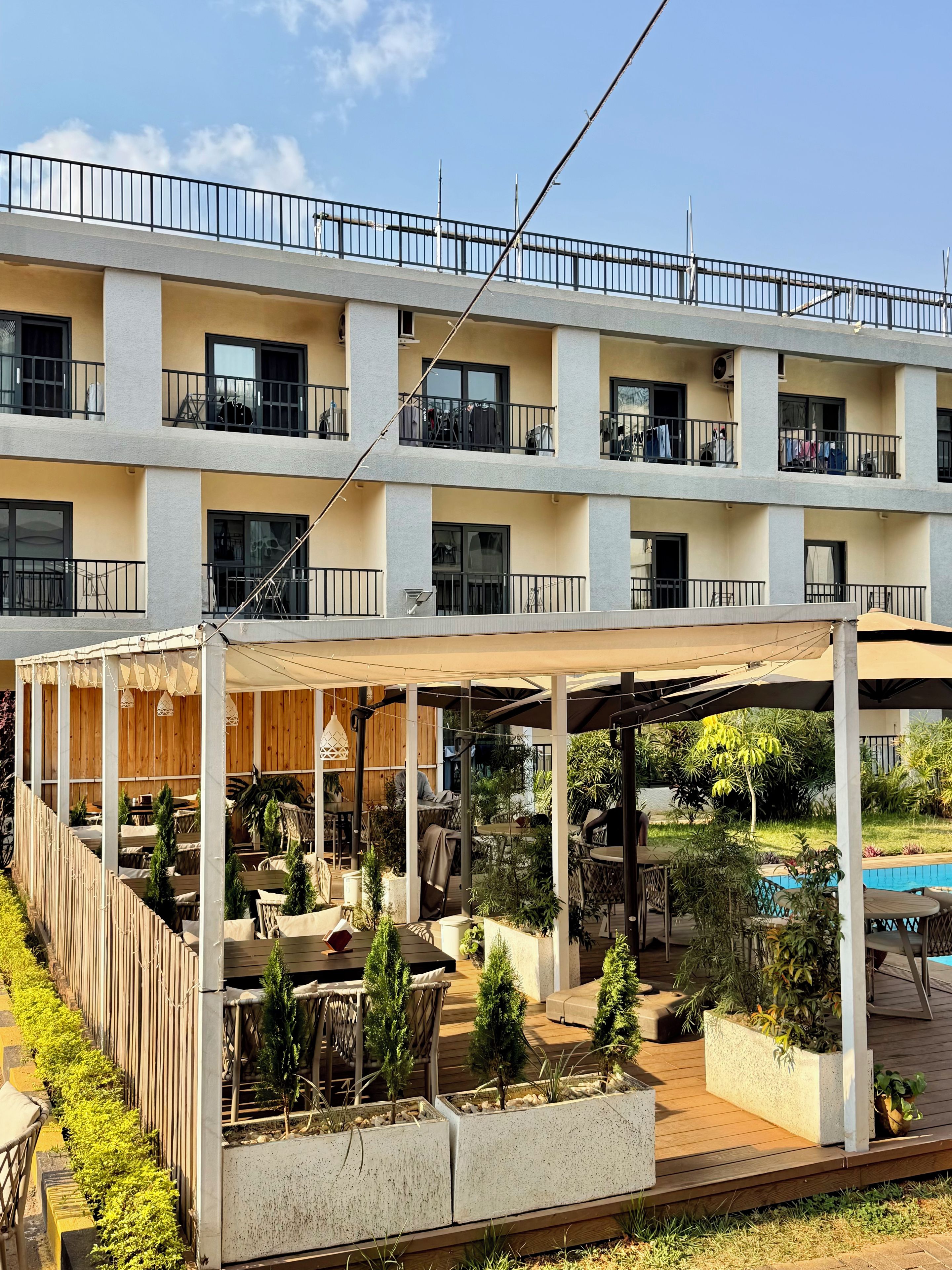 A multi-story hotel with outdoor seating areas, a pool, and a balcony with clothes drying.