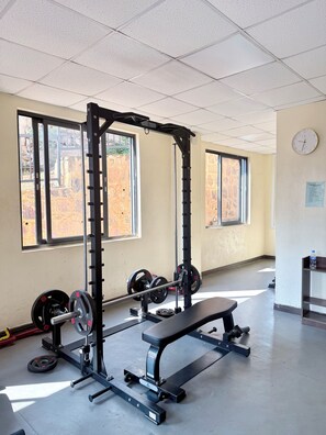 A gym with weightlifting equipment, large windows, and a clock on the wall. - Phoenix Apartment by LINK (Kigali)