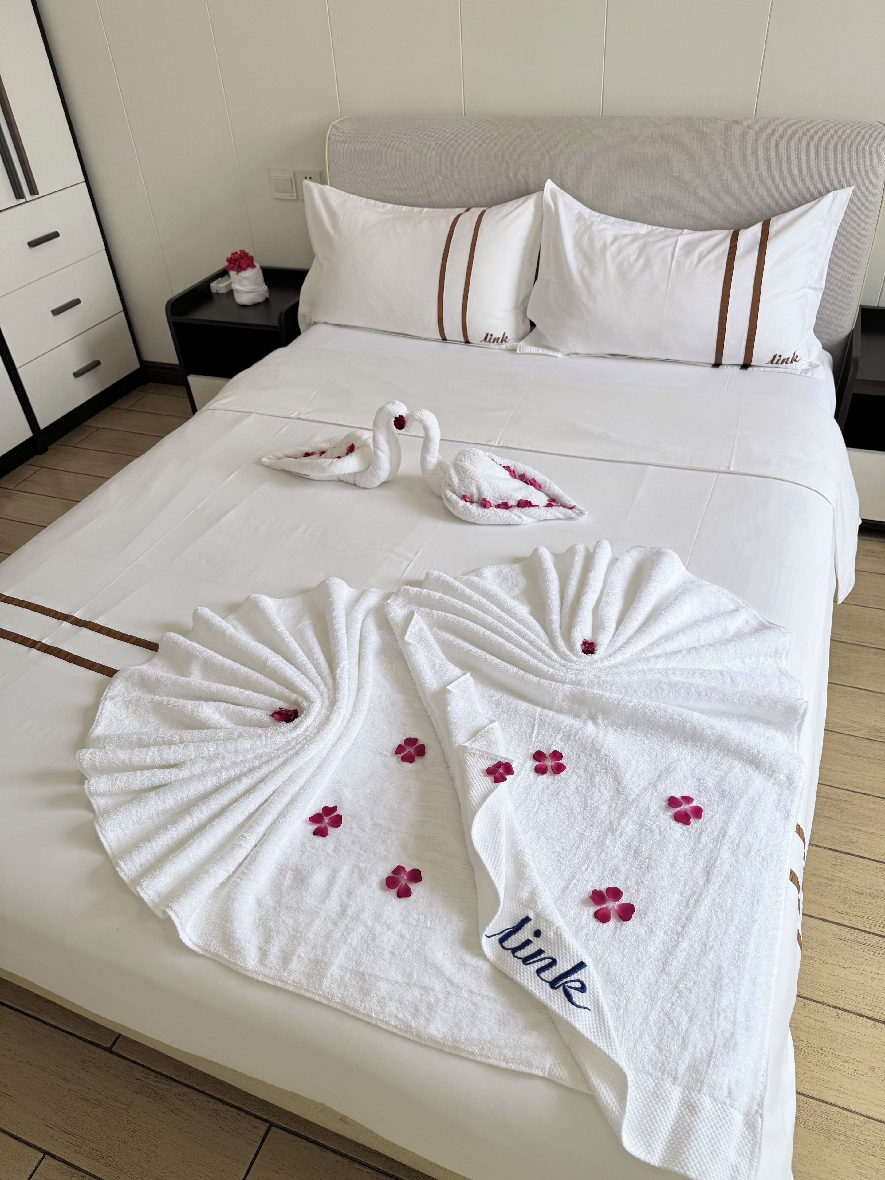 A neatly made bed with white linens and decorative swan towels.