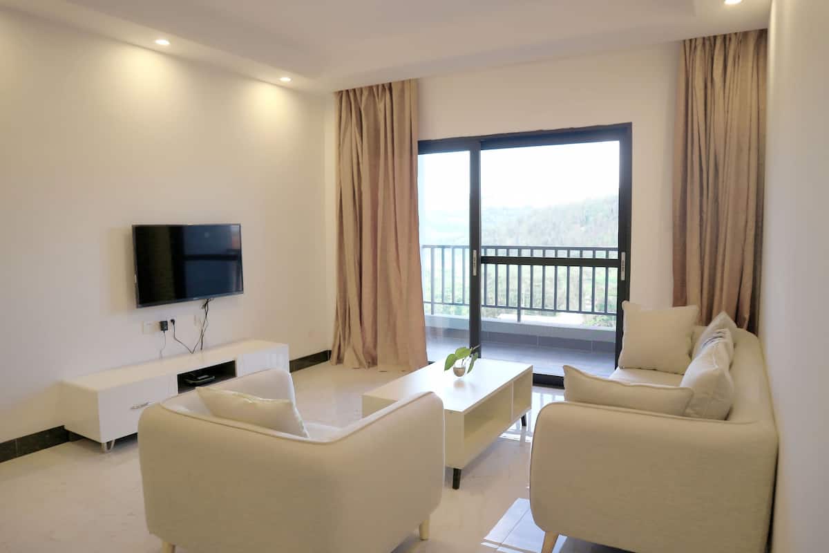 Una sala de estar moderna con un televisor de pantalla plana, un sofá blanco, una mesa de centro y un balcón con cortinas.