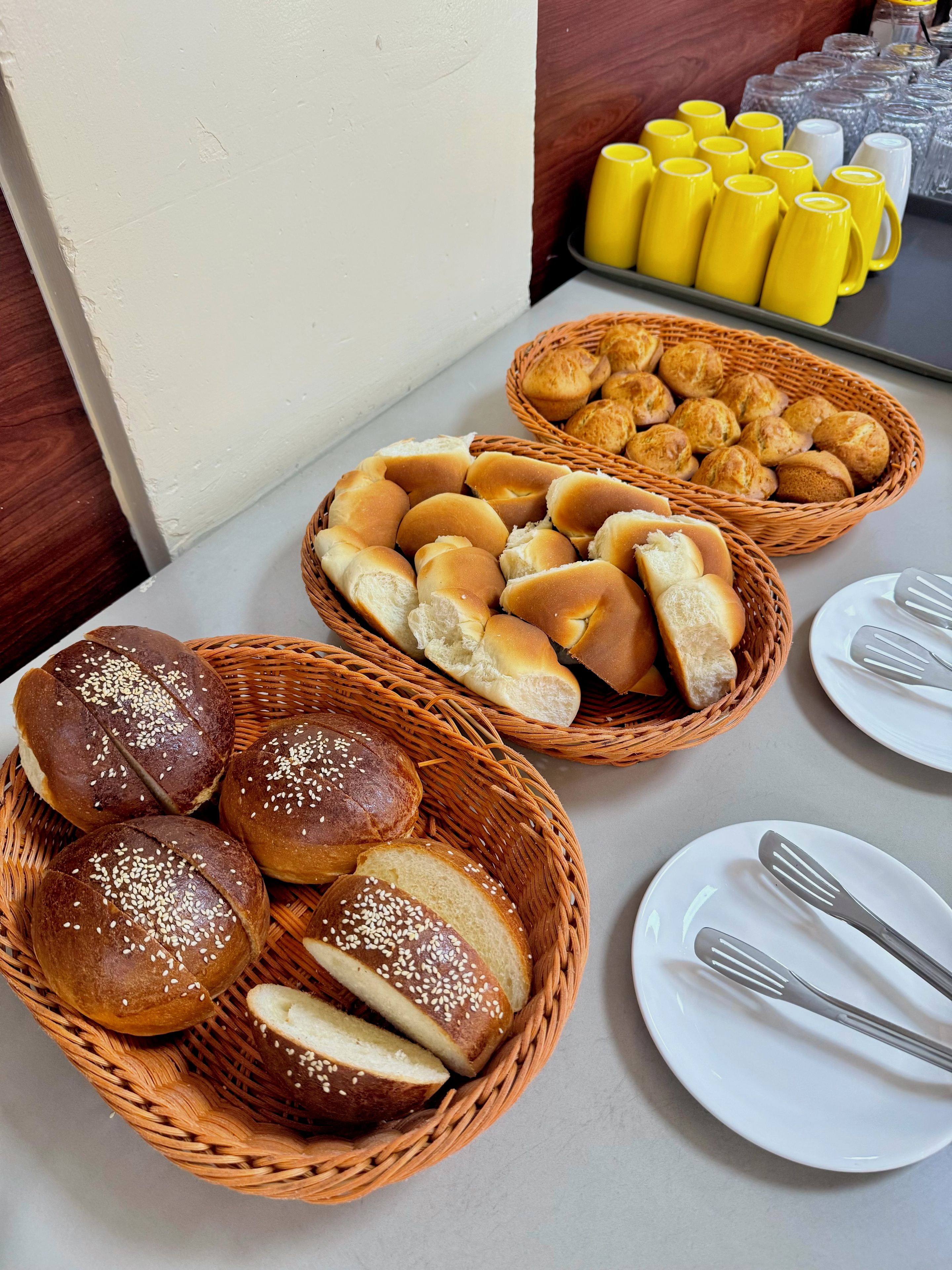 Un tavolo con cesti di pane e un vassoio di tazze gialle.