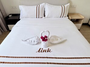A hotel room with a neatly made bed featuring a towel swan centerpiece and the name 'Aink' embroidered on the bedspread. - Phoenix Apartment by LINK (Kigali)