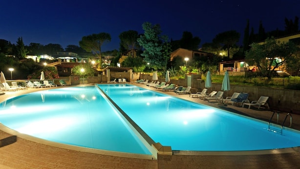 Una grande piscina esterna con diverse corsie, circondata da lettini e ombrelloni.