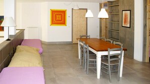 A room with a bed, a dining table with chairs, a lamp, and a wall with a geometric painting. - Cosy apartment in villa for 11 people with pool, terrace and pets allowed (Guardistallo)