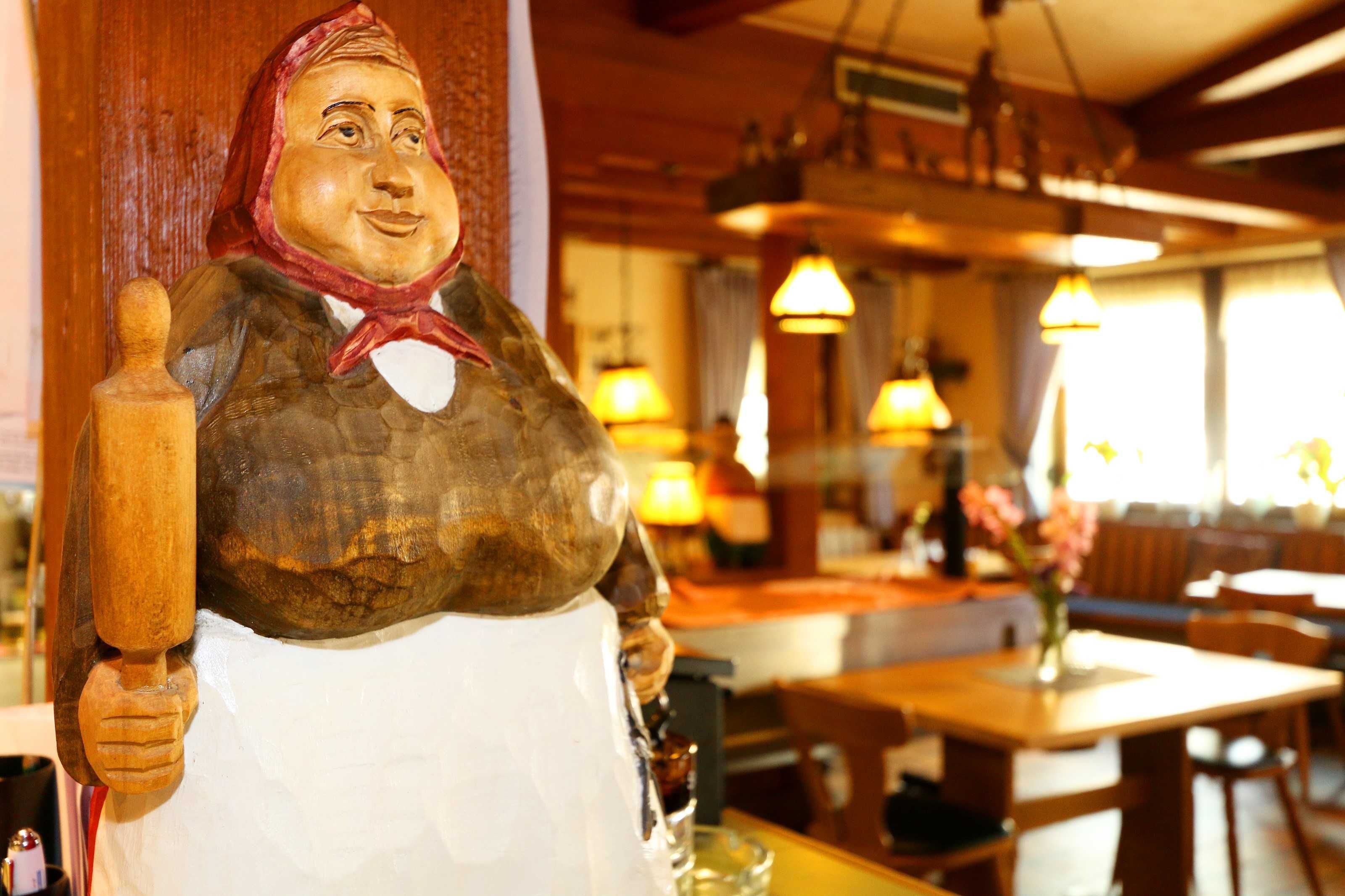 Een houten standbeeld van een persoon met een deegroller, een houten tafel en een eetruimte met stoelen en tafels.