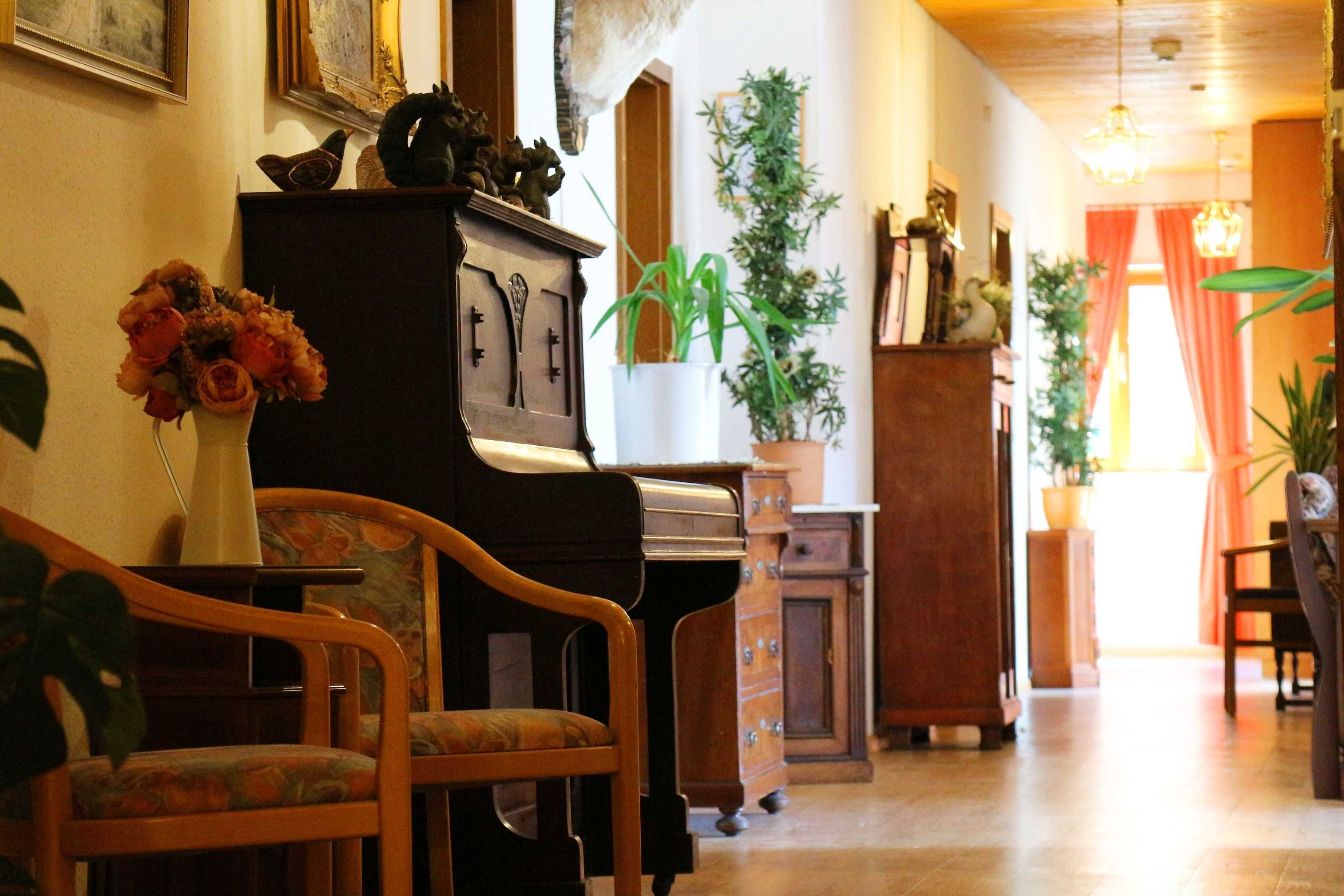 Ein Zimmer mit einem Klavier, einem Holzstuhl, einer Blumenvase und einem Topfpflanzen.