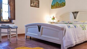 A bedroom with a bed, a chair, a yellow rug, a painting, and a window. - Nice apartment in villa for 2 people with pool, WIFI, TV and patio (Lajatico)