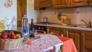 A kitchen with wooden cabinets, a stove, a coffee maker, and a table with a tablecloth and fruit basket. - Nice apartment in villa for 2 people with pool, WIFI, TV and patio (Lajatico)