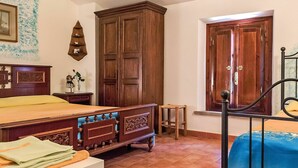 A bedroom with a wooden bed, a wardrobe, a small stool, and a window with a wooden door. - Beautiful apartment in villa for 4 people with WIFI, pool, TV and patio (Lajatico)