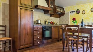 A kitchen with wooden cabinets, a stove, and a dining area with chairs and a table. - Beautiful apartment in villa for 4 people with WIFI, pool, TV and patio (Lajatico)