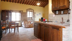 A rustic kitchen with a stone wall, wooden cabinets, and a tiled backsplash. - Cosy apartment in villa for 2 guests with WIFI, TV, patio and pets allowed (Roccastrada)
