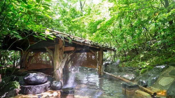 Un ponte in legno che sovrasta un ruscello limpido, con rocce e una struttura in legno sulla sinistra.