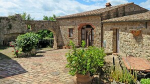 A stone building with a courtyard, featuring a brick pathway, a wooden table, and potted plants. - Cosy apartment in villa for 3 guests with WIFI, TV, patio and pets allowed (Roccastrada)