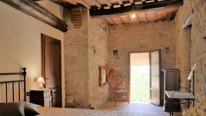 A rustic bedroom with a bed, a chair, a desk, and a view of the outside. - Cosy apartment in villa for 3 guests with WIFI, TV, patio and pets allowed (Roccastrada)