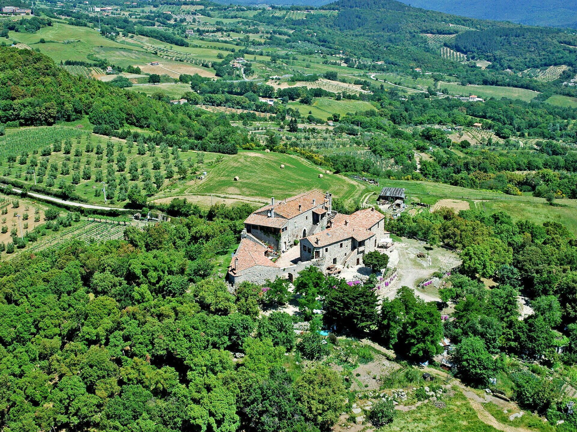 A historic stone building with a courtyard, surrounded by lush greenery and vineyards.